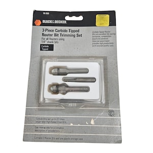 May include: A 3-piece carbide-tipped router bit trimming set by Black & Decker. The set includes three router bits and a plastic storage case. The package is gray and black with product information and the text "3-Piece Carbide-Tipped Router Bit Trimming Set".