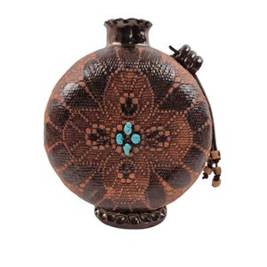 May include: A round, brown ceramic flask with a textured lace-like pattern and a dark brown glaze. The center features four small, bright turquoise stones arranged in a cross shape. A leather cord with wooden beads is attached to the side.