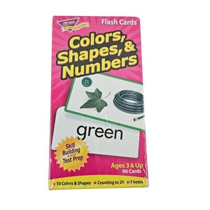 May include: A package of flash cards for children, featuring the title "Colors, Shapes, & Numbers." The cards are designed for ages 3 and up and include 96 cards. The package is pink and has a green card with the word "green" on it.