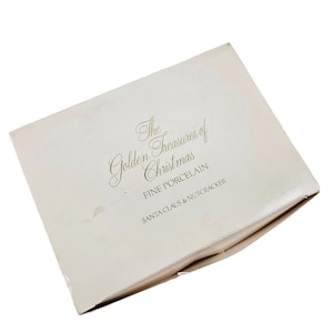 May include: A white box with gold lettering that reads "The Golden Treasures of Christmas Fine Porcelain Santa Claus & Nutcracker".