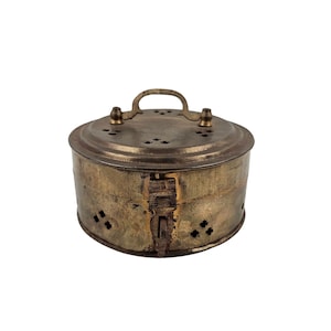 May include: A round, brass container with a hinged lid and a handle. The container has decorative cutouts and a worn, aged finish.