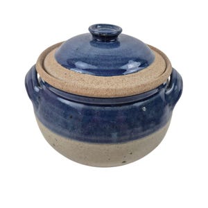 Puede incluir: Una cazuela de cerámica azul y beige con tapa. El plato tiene dos asas y una tapa con un pequeño pomo. La tapa tiene un borde beige. El plato es adecuado para cocinar y servir.