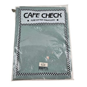 Puede incluir: Un mantel de algodón puro verde salvia empaquetado. La etiqueta dice "CAFE CHECK" con un borde a cuadros blanco y negro. El tamaño es de 152 cm x 259 cm oblongo. La marca "BARDWIL LINENS" también es visible.