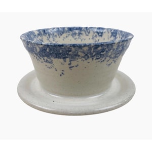 Puede incluir: Un filtro de café de cerámica blanca con un esmalte moteado azul. El filtro tiene un platillo.