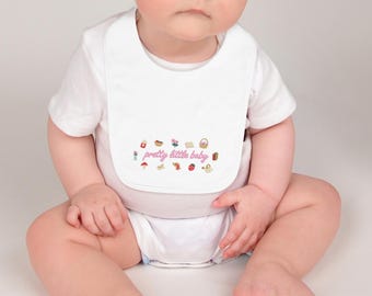 Könnte beinhalten: Ein weißes Baby-Lätzchen mit dem rosa Schriftzug "pretty little baby". Das Lätzchen ist mit kleinen, farbenfrohen Illustrationen verziert. Das Baby trägt einen weißen Body.