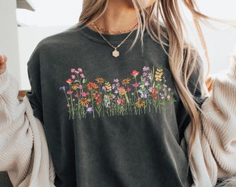 May include: A dark gray sweatshirt featuring a colorful floral design across the chest. The embroidered flowers include shades of pink, orange, yellow, and purple. The word "Pepper" is in the top left corner.