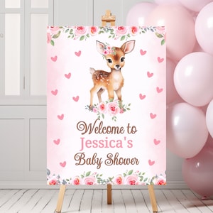 May include: Pink and white baby shower welcome sign with a floral border and a cute cartoon fawn wearing a flower crown. The sign says "Welcome to Jessica's Baby Shower".