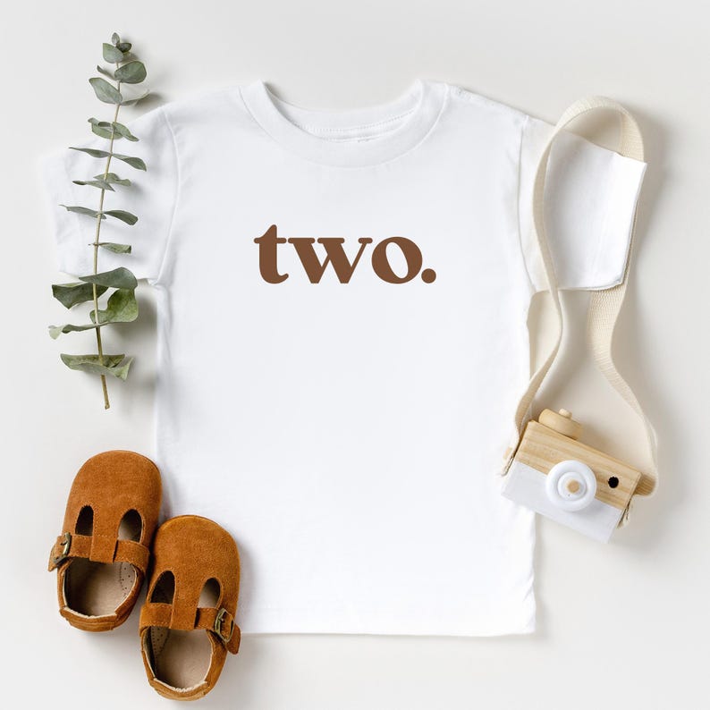 May include: White t-shirt with brown text that says "two".