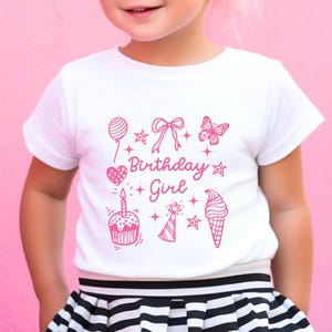 May include: White t-shirt with a pink graphic design that says "Birthday Girl" and features a cupcake, ice cream cone, butterfly, balloon, and stars.