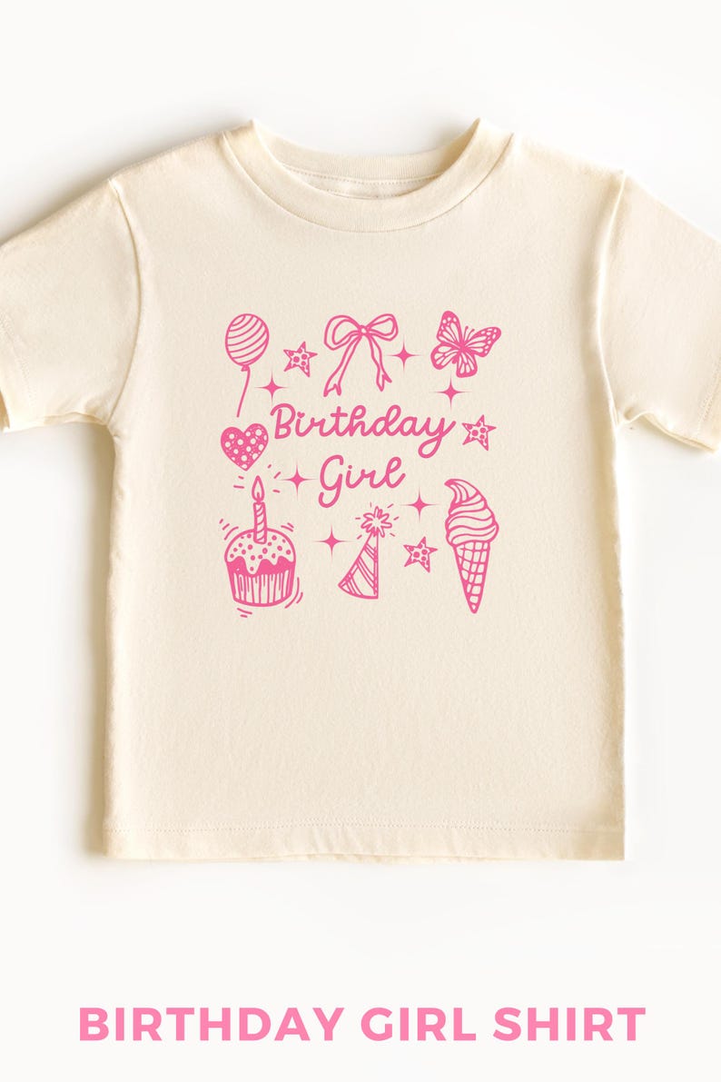 May include: A cream colored t-shirt with a pink graphic design that says "Birthday Girl" and includes a birthday cake, a party hat, a balloon, a heart, a butterfly, and an ice cream cone.