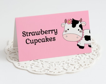 May include: Pink card with a black and white cow illustration wearing a pink flower and a pink beaded necklace. The text "Strawberry Cupcakes" is printed in black.