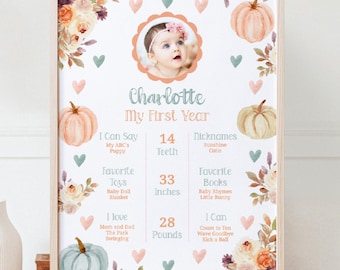 May include: A white and peach pumpkin themed first birthday chart with a photo of a baby girl. The chart includes the baby's name, Charlotte, and details about her first year, including her age, height, weight, favorite toys, books, and activities.