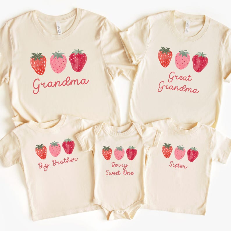May include: A collection of cream-colored t-shirts and a onesie, each adorned with a strawberry design and a family-related title. The shirts feature the words "Grandma", "Great Grandma", "Big Brother", and "Sister", while the onesie says "Berry Sweet One".