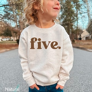 May include: A light beige sweatshirt with the word "five" in brown lettering. The sweatshirt is made of a soft material and is suitable for children. The words "Natural Heather" are printed at the bottom of the image.