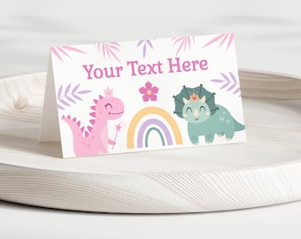 Puede incluir: Una tarjeta blanca con un dinosaurio rosa con una corona y sosteniendo una varita mágica, un dinosaurio azul con una corona y un arcoíris. El texto "Your Text Here" está en la parte superior de la tarjeta.