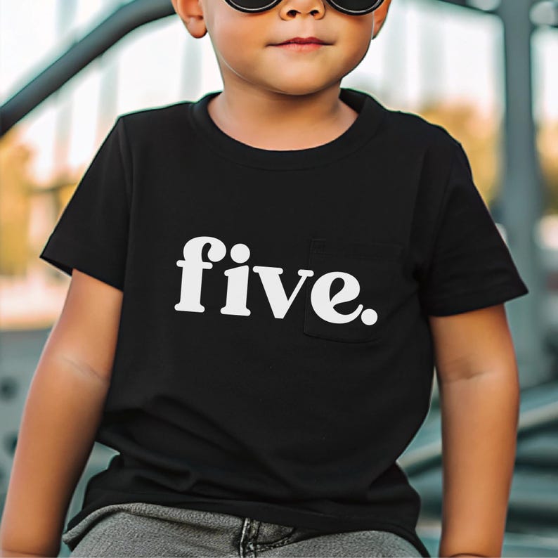 May include: Black t-shirt with a white pocket and the word "five." printed in a bold, sans-serif font. The shirt is short-sleeved and appears to be made of a soft material.
