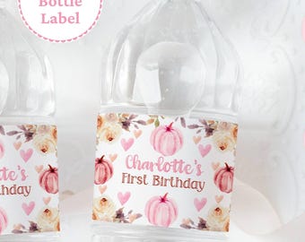 May include: Clear plastic water bottles with labels featuring pink pumpkins, hearts, and floral accents. The label reads "Charlotte's First Birthday." The bottles have white caps and are designed for a birthday celebration.