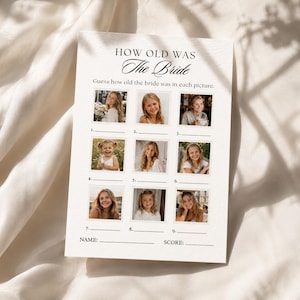 Può includere: Una scheda bianca con il testo "HOW OLD WAS The Bride" e "Indovina quanti anni aveva la sposa in ogni foto." Nove piccole foto sono disposte in una griglia, con spazi per nomi e punteggi in basso. La scheda è su un tessuto bianco.