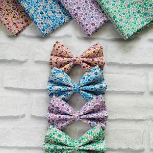 May include: Five bow ties made from floral patterned fabric. The bow ties are stacked on top of each other. The bow ties are in the following colors: orange, blue, purple, green, and red.
