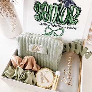 Peut inclure: Une bo&icirc;te cadeau blanche remplie d'articles sur le th&egrave;me de la remise de dipl&ocirc;me. Comprend une trousse de maquillage verte, des chouchous, un miroir compact, un baume &agrave; l&egrave;vres et un gobelet personnalis&eacute;. Le couvercle de la bo&icirc;te porte l'inscription "Senior" en vert et l'ann&eacute;e "twenty twenty-seven".