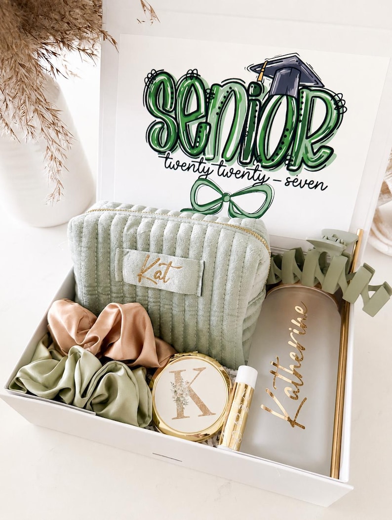 Peut inclure: Une bo&icirc;te cadeau blanche remplie d'articles sur le th&egrave;me de la remise de dipl&ocirc;me. Comprend une trousse de maquillage verte, des chouchous, un miroir compact, un baume &agrave; l&egrave;vres et un gobelet personnalis&eacute;. Le couvercle de la bo&icirc;te porte l'inscription "Senior" en vert et l'ann&eacute;e "twenty twenty-seven".