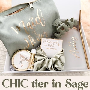May include: A sage green gift box containing a makeup bag with gold script reading "Maid of Honor", a compact mirror, lip balm, a scrunchie, a water bottle with a gold straw, and a card. The text "CHIC tier in Sage" is at the bottom.