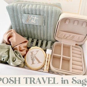 May include: A sage green travel set including a quilted cosmetic bag with the name "Kat", a jewelry case, scrunchies, hair clips, a compact mirror, and lip balm. The compact mirror features the letter "K" with floral detailing. The set is presented in a white box.