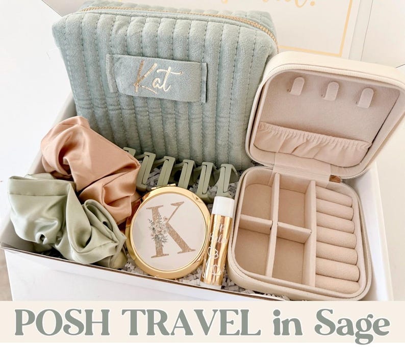May include: A sage green travel set including a quilted cosmetic bag with the name "Kat", a jewelry case, scrunchies, hair clips, a compact mirror, and lip balm. The compact mirror features the letter "K" with floral detailing. The set is presented in a white box.