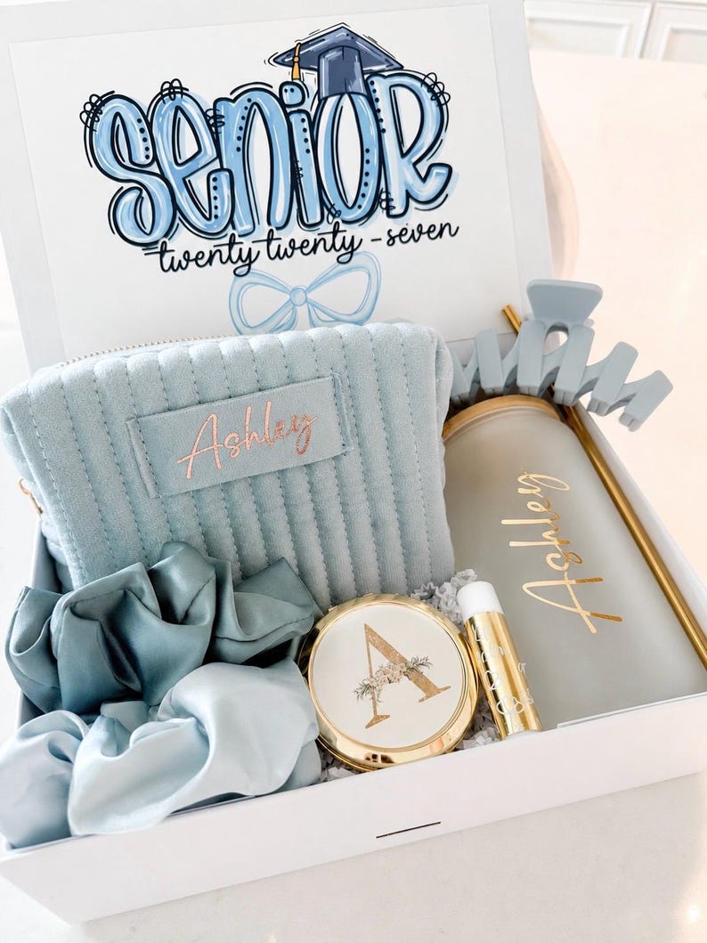 Peut inclure: Coffret cadeau blanc contenant une trousse de maquillage bleu clair, des chouchous, un miroir compact, un baume &agrave; l&egrave;vres et un gobelet. Le couvercle de la bo&icirc;te porte l'inscription "Senior" en bleu, avec le texte "twenty twenty - seven".