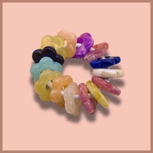 Può includere: Un sonaglio colorato per bambini con perline a forma di fiore in vari colori, tra cui giallo, arancione, viola e blu. Le perline sono infilate su un anello bianco. Il sonaglio è progettato per neonati e bambini piccoli.