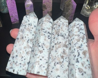 May include: Five white and gray granite crystal points, also known as white granite, are arranged in a row. The points are polished and have a smooth, shiny surface.