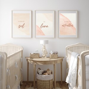 May include: Three framed prints with watercolor-style backgrounds in shades of peach and cream. The prints feature Spanish text that reads "tu eres mi sol", "mi luna", and "y todas mis estrellas". The prints are displayed above a wooden table with a lamp and baskets.