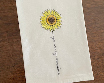 May include: White kitchen towel with a yellow sunflower illustration and the text "you are my sunshine" in black cursive.