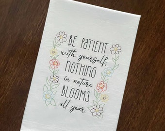 May include: White kitchen towel with a floral border and the text "BE PATIENT with yourself. NOTHING in nature BLOOMS all year."