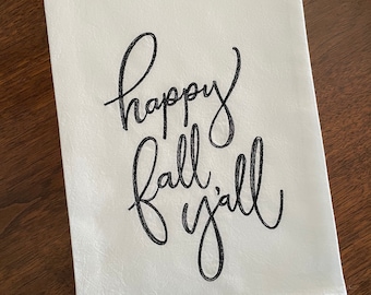 May include: White kitchen towel with black embroidered text that reads "happy fall y'all".