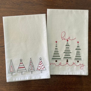 Puede incluir: Dos toallas de cocina blancas con árboles de Navidad bordados y el texto "be merry".