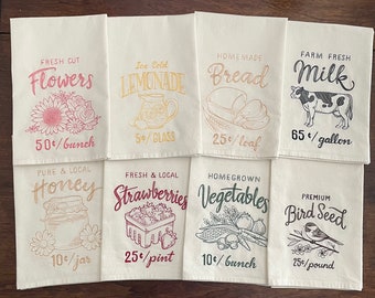 May include: Eight white tea towels with different designs and prices. The designs include flowers, lemonade, bread, milk, honey, strawberries, vegetables, and bird seed.