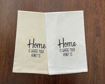 May include: Two white tea towels with a honeycomb pattern and the text "Home is where your honey is" in black.
