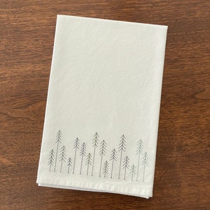 May include: White kitchen towel with a green embroidered design of a row of pine trees.