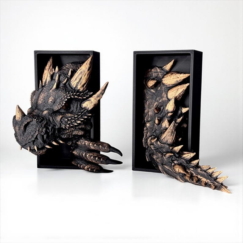 May include: Two dragon head wall sculptures. The dragon heads are dark brown with tan horns and spikes. The sculptures are mounted in black rectangular frames, with one head and one tail extending out.