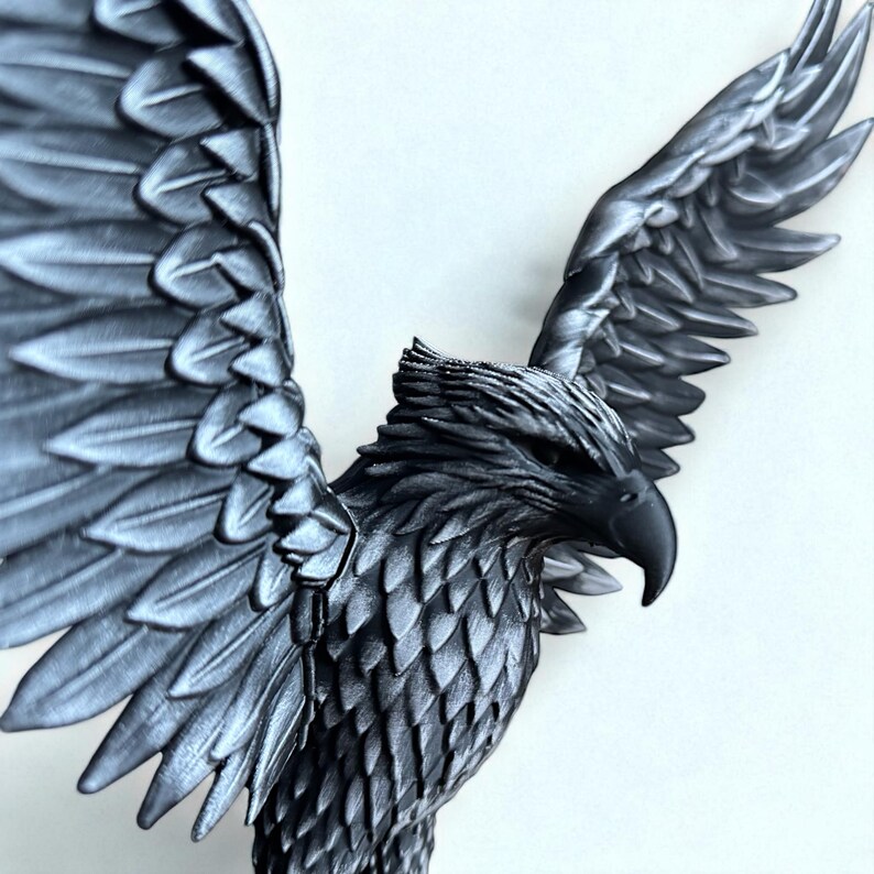 May include: A detailed, metallic gray sculpture of an eagle with outstretched wings. The eagle's feathers are intricately carved, and its beak is sharply defined. The sculpture is set against a plain white background, highlighting the bird's form.