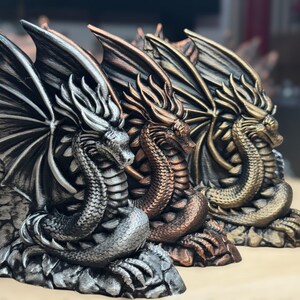 May include: Three dragon bookends in different metallic finishes: silver, copper, and gold. Each dragon is curled up with its wings spread out, creating a decorative and functional bookend set.