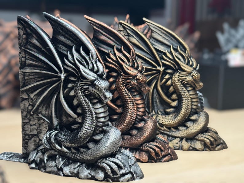 May include: Three dragon bookends in different metallic finishes: silver, copper, and gold. Each dragon is curled up with its wings spread out, creating a decorative and functional bookend set.