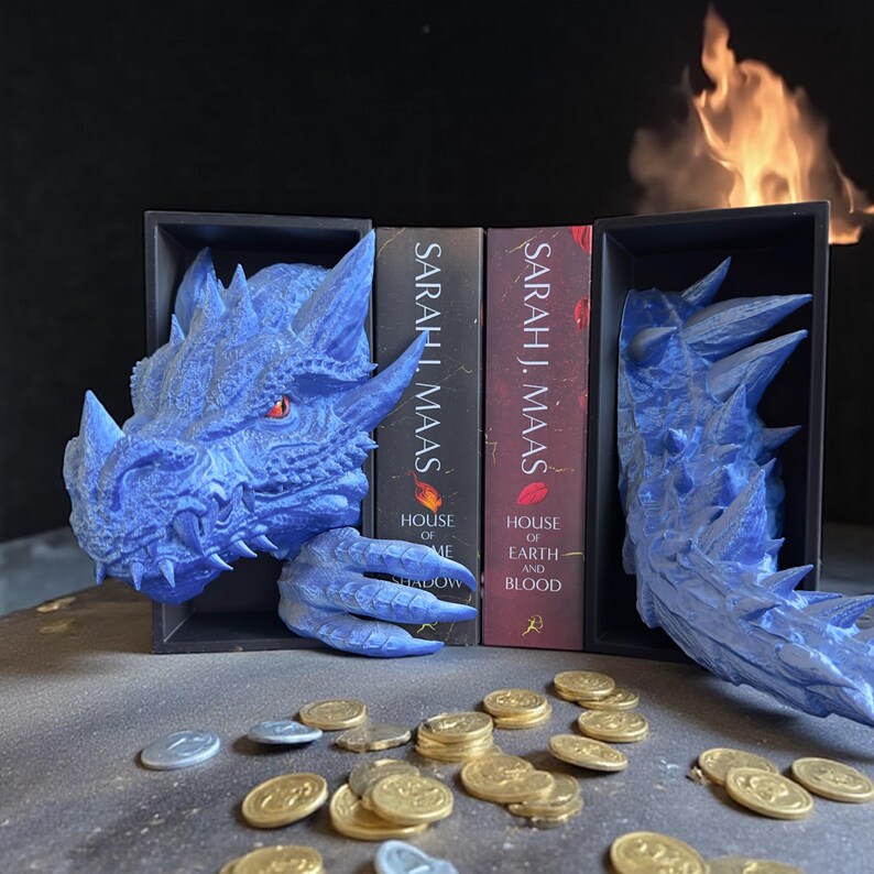 May include: A blue dragon bookend set with a detailed head and tail design. The bookends are holding two books by Sarah J. Maas. Gold coins are scattered in front of the bookends. The bookends are in a black box.
