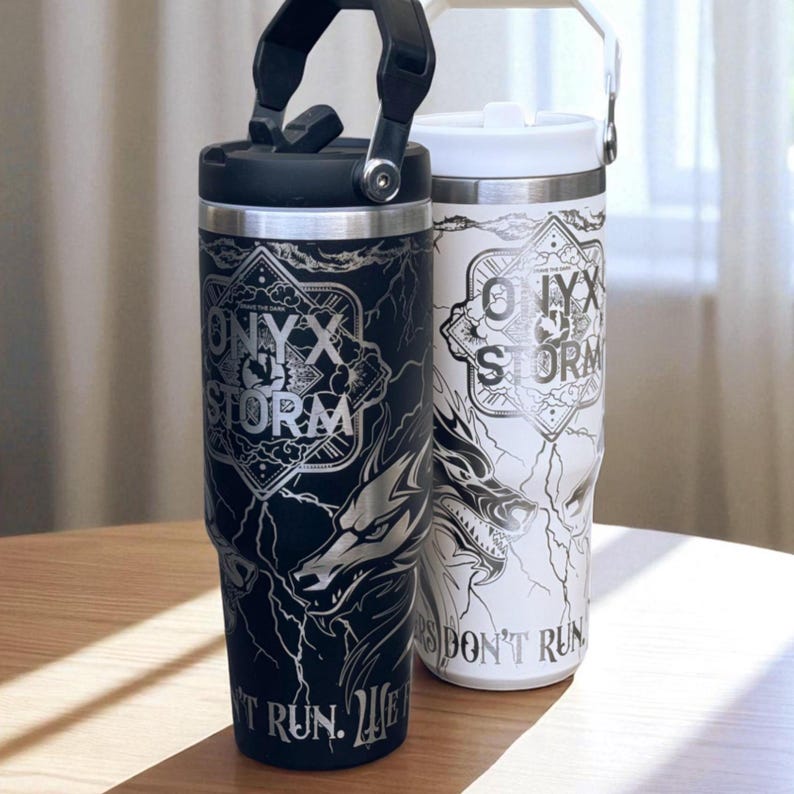 May include: Two insulated tumblers, one black and one white, featuring the text "ONYX STORM" and a wolf design. The black tumbler has a black handle and lid, the white one has a white handle and lid. The text "THEY DON'T RUN" is also visible.