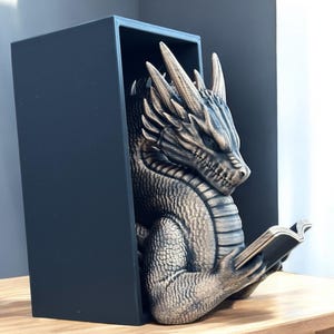 May include: A gold dragon bookend with a black base, holding a book in its claws. The dragon is detailed with scales and has a fierce expression.