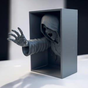 May include: A gray 3D printed sculpture of a hooded figure with a skeletal face reaching out from a gray box.