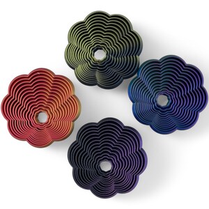 May include: Four flower-shaped decorative objects in red, green, blue, and purple. Each has a central hole and concentric layered design. The objects are arranged on a white background.