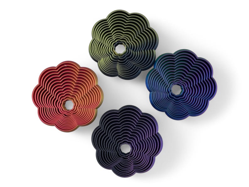 May include: Four flower-shaped decorative objects in red, green, blue, and purple. Each has a central hole and concentric layered design. The objects are arranged on a white background.