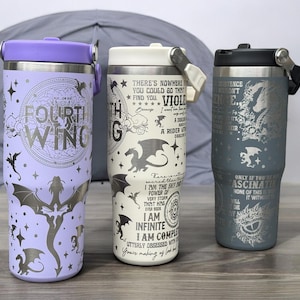 May include: Three stainless steel travel tumblers with different dragon designs and quotes. The purple tumbler has a dragon with the words "Fourth Wing" on it. The white tumbler has a dragon with the words "I am the sky, the power of every storm that hits, I am infinite, I am complete" on it. The gray tumbler has a dragon with the words "Only if you are fascinated by none of this will you die" on it.